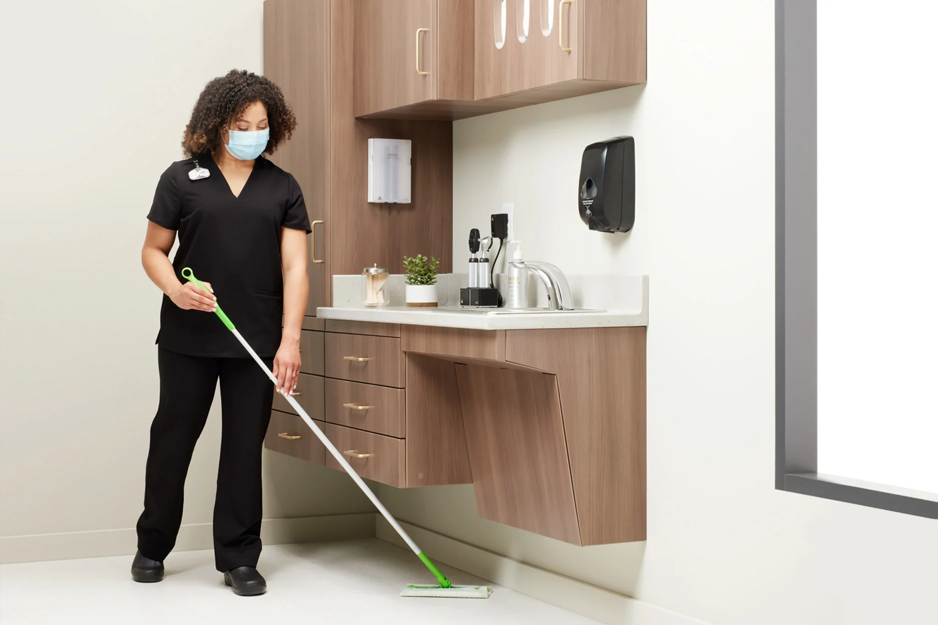 nurse cleaning under cabinets in a medical exam room