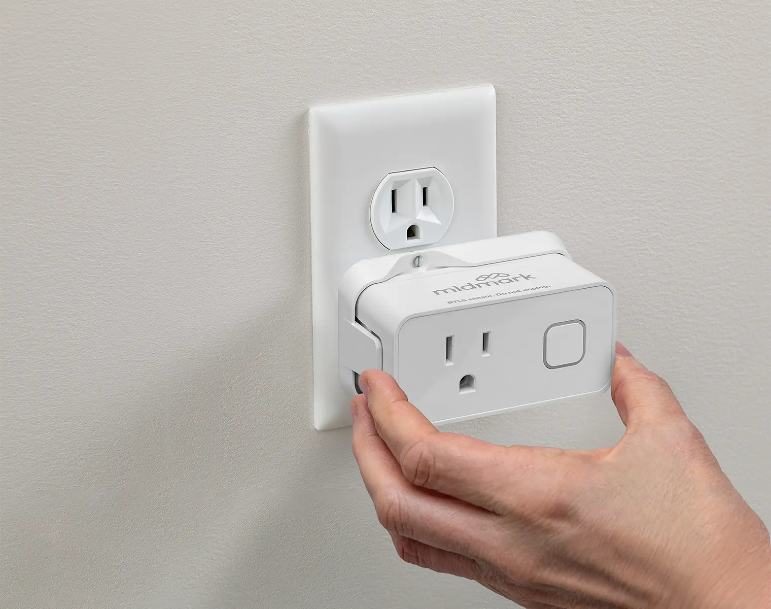 a hand plugging in a white Midmark rtls plug-in sensor into a standard wall outlet