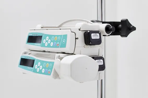 Two stacked automated infusion pumps mounted to an IV pole, each equipped with a black Midmark RTLS asset tracking hardware tag.