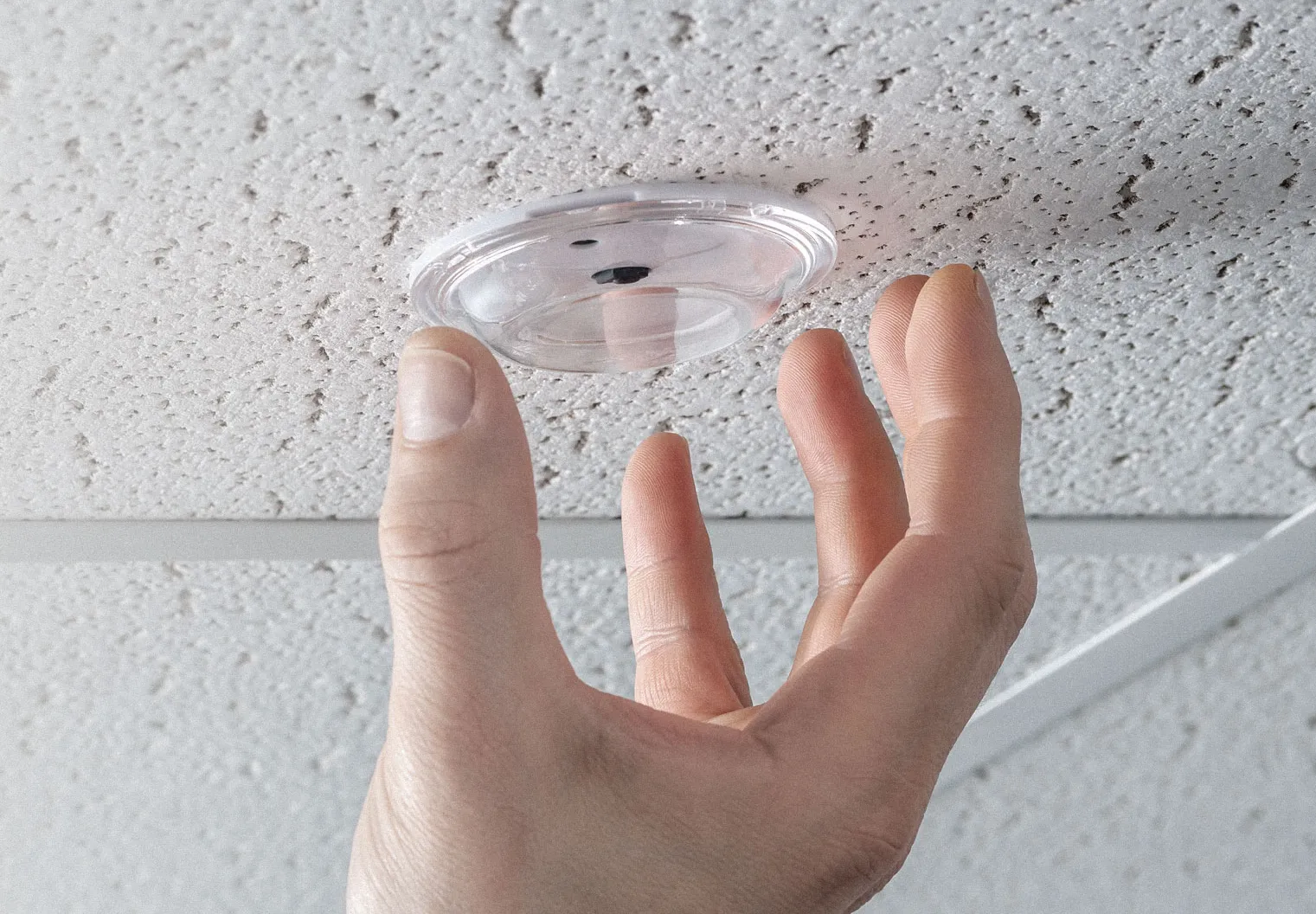 A hand reaches up to adjust or install a small, circular, clear Midmark RTLS sensor mounted flush against a textured ceiling tile.