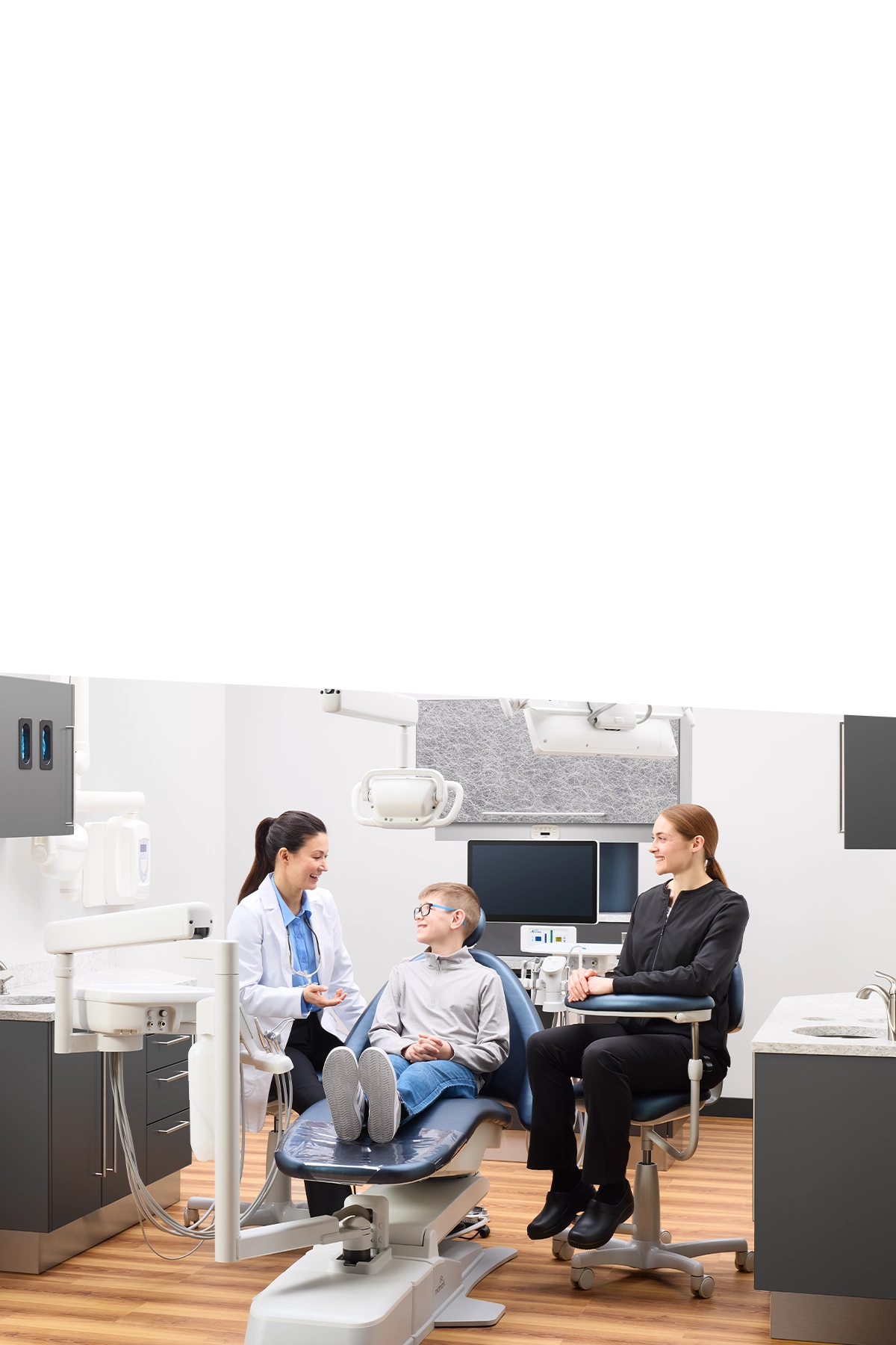 Young male dental patient speaking with dentist and dental assistant in operatory
