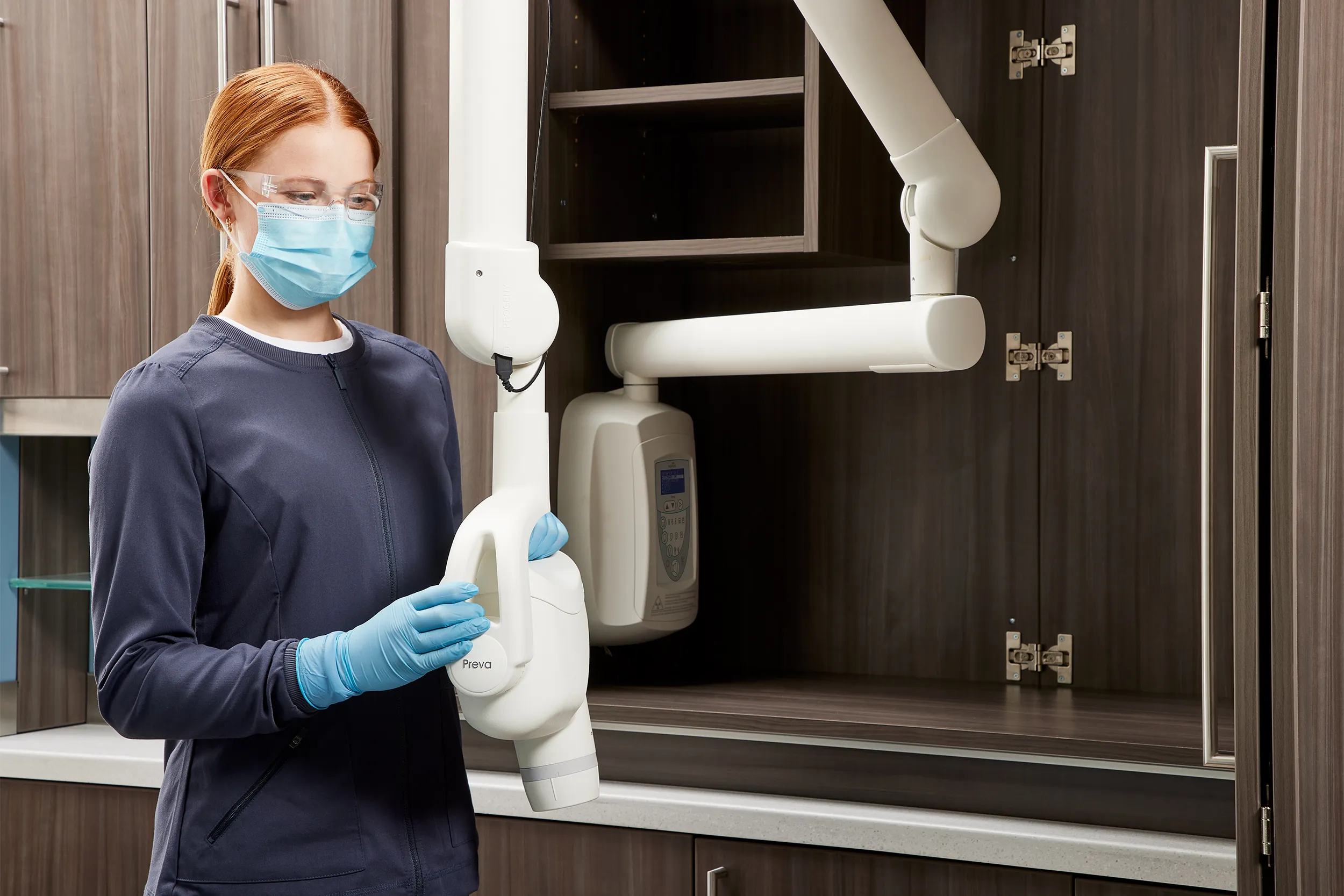 Dental assistant preparing an intraoral X-ray machine for patient imaging in a modern dental operatory.