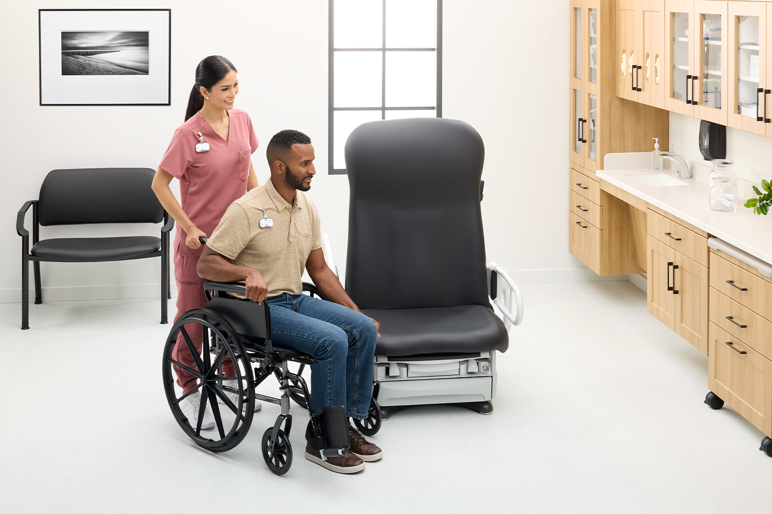 Caregiver assists a patient using a wheelchair beside an examination chair in a clinic room.